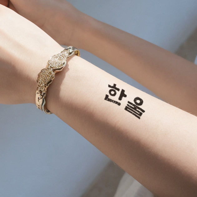 An arm with a Sino-Korean word temporary tattoo on the forearm, accented by sunlight and a delicate gold bracelet.