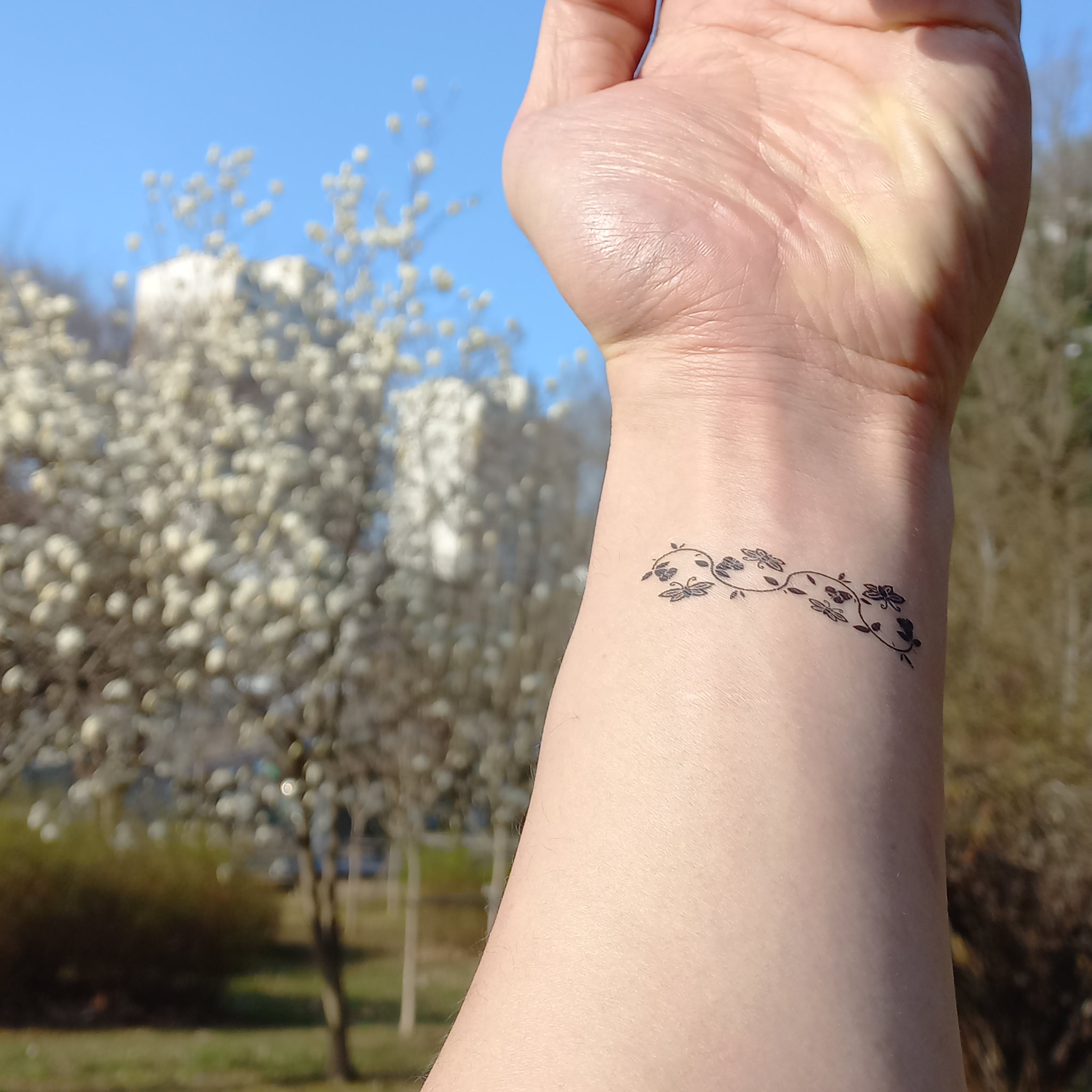 A wrist adorned with a delicate floral temporary tattoo, with blooming trees in the background, symbolizing spring.